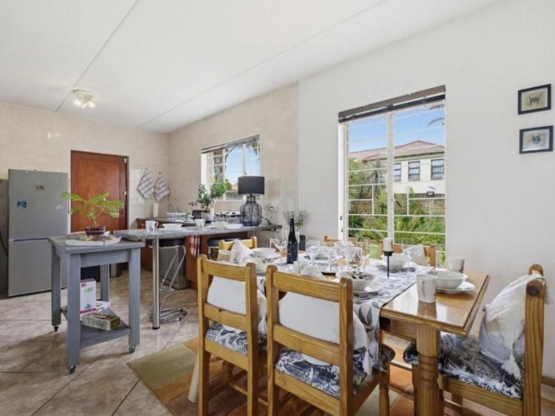 Open-plan kitchen and dining area featuring tiled flooring, functional cabinetry, and a breakfast bar, with natural light provided by large windows.