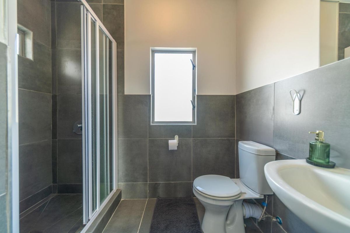 A modern bathroom featuring a glass-enclosed shower, a white toilet, and a wall-mounted washbasin with grey tiled finishes.