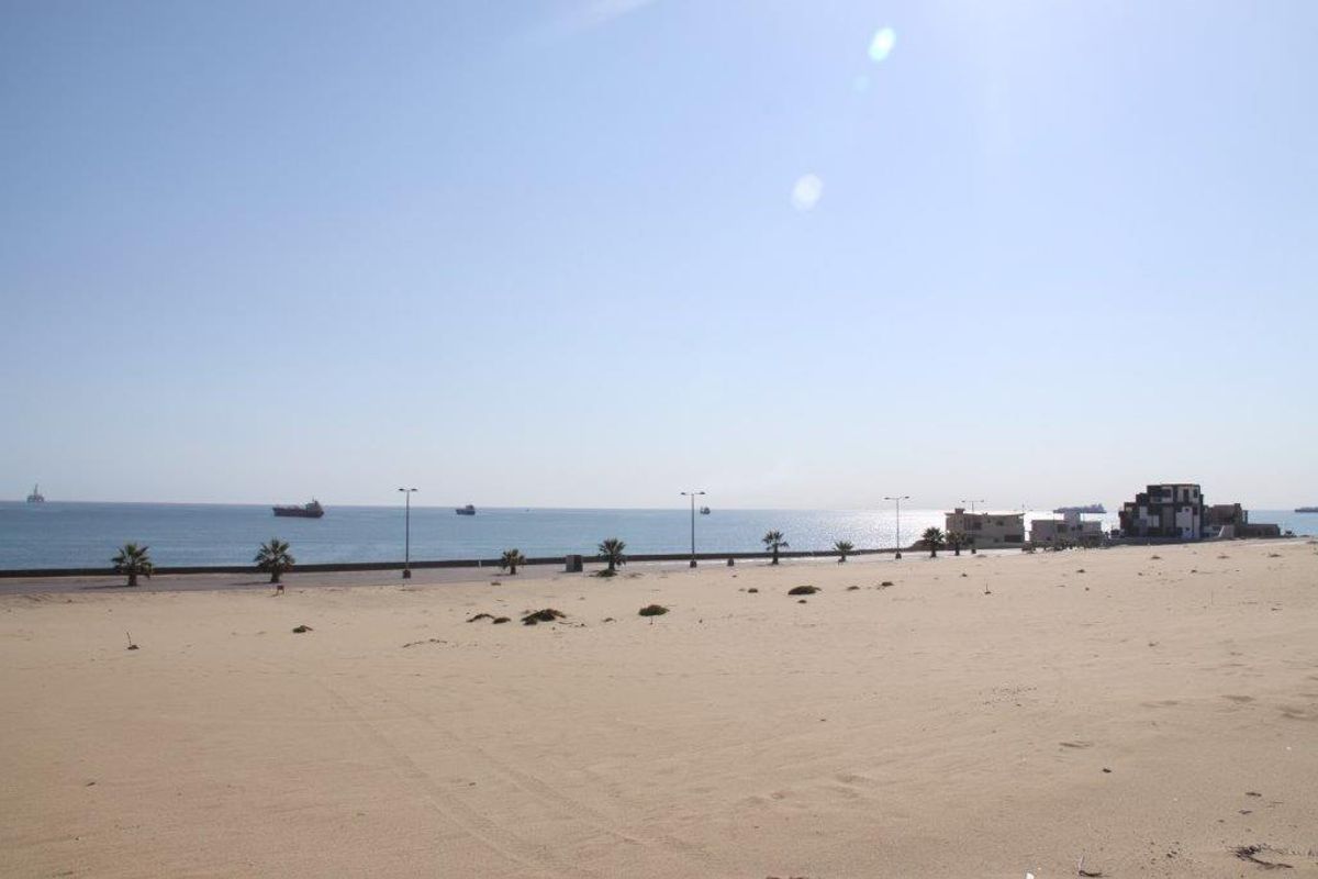 A wide-angle view of the coastal landscape and beachfront area, showcasing the open sandy terrain and proximity to the ocean.