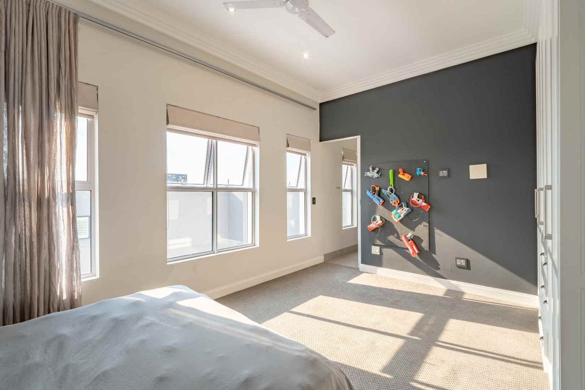 A bright bedroom featuring neutral carpeting, a dark accent wall, built-in cabinetry, and large windows with fitted blinds.