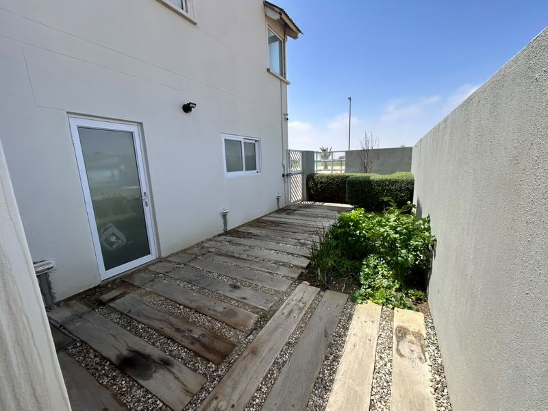 A rear exterior area featuring a timber sleeper pathway set in gravel, bordered by a boundary wall and a small garden bed.