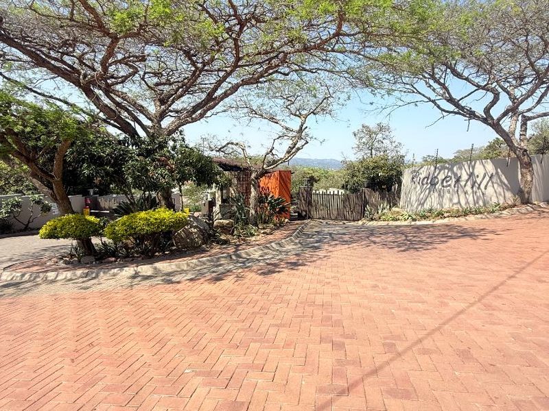 View of the entrance to the residential estate featuring a paved driveway, security gate, and established landscaping.