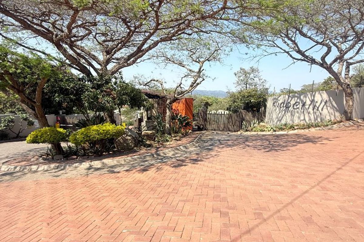 View of the entrance to the residential estate featuring a paved driveway, security gate, and established landscaping.