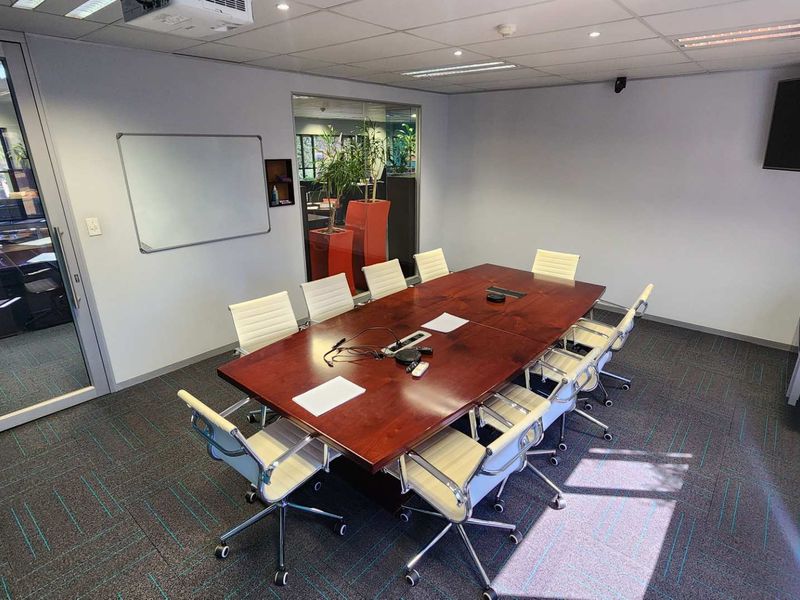 A professional office meeting room featuring a large boardroom table, glass partition walls, suspended ceiling, and modern carpet tiles.