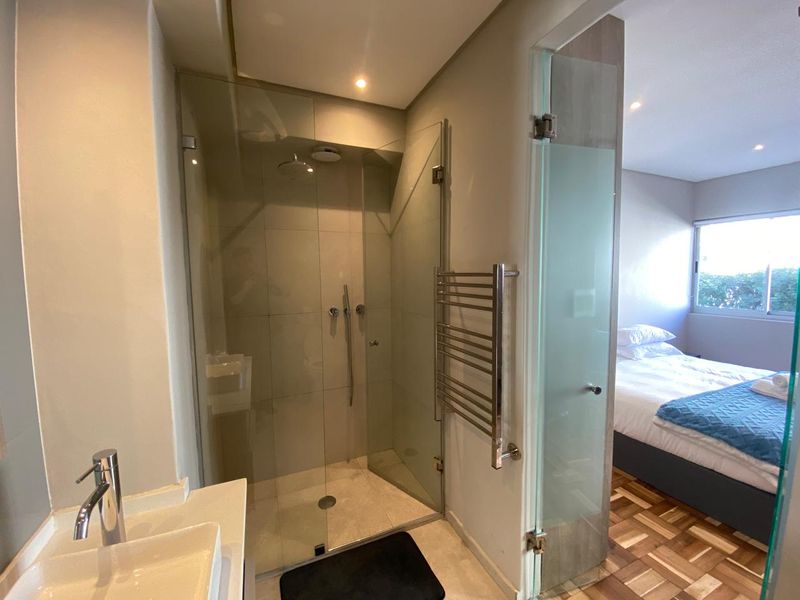 Modern bathroom featuring a glass-enclosed shower, contemporary vessel sink, and a heated towel rail, with direct access to the adjacent bedroom.