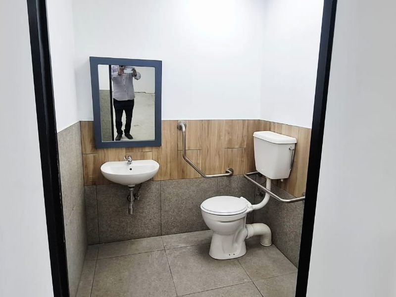 A clean, functional accessible bathroom featuring a wall-mounted basin, toilet, and safety grab rails with neutral tiled finishes.