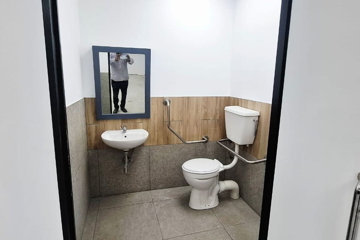 A clean, functional accessible bathroom featuring a wall-mounted basin, toilet, and safety grab rails with neutral tiled finishes.