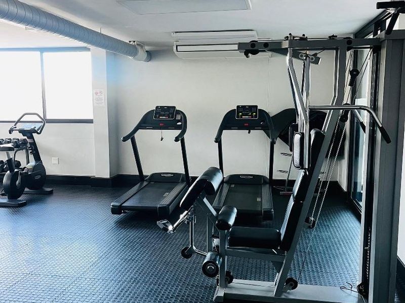 A well-maintained apartment gym facility featuring durable rubber flooring, exposed industrial ducting, and integrated air conditioning for climate control.