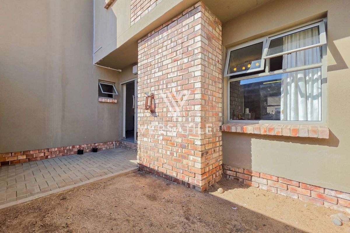 A rear exterior view of the townhouse featuring a paved patio area, exposed brick facade detailing, and aluminium window frames.