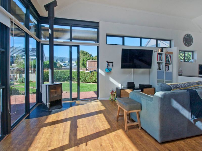 Bright open-plan living area featuring vaulted ceilings, laminate flooring, a modern freestanding fireplace, and expansive glass sliding doors opening to the garden.