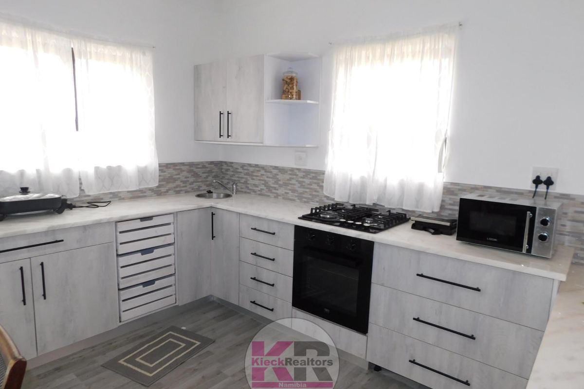 A modern kitchen featuring light wood-grain cabinetry, stone-look countertops, a built-in oven, gas hob, and a tiled backsplash.