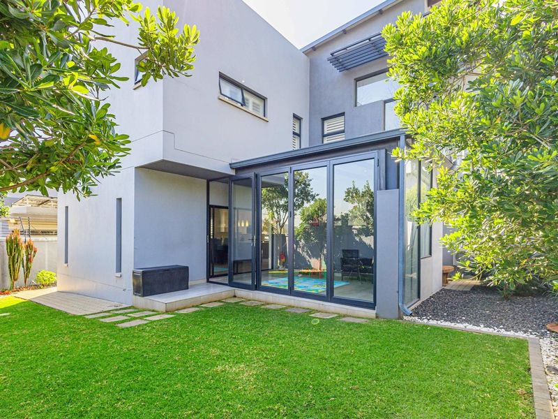 Modern rear elevation featuring large glass sliding doors, clean architectural lines, and a well-maintained private garden area.