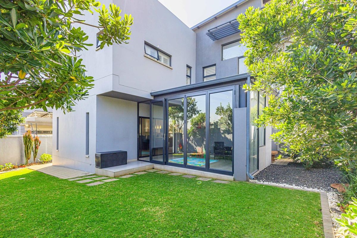 Modern rear elevation featuring large glass sliding doors, clean architectural lines, and a well-maintained private garden area.