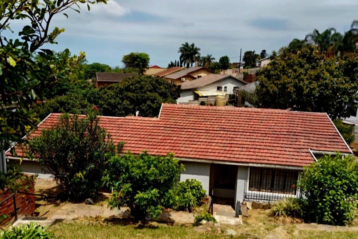 An elevated view of the rear of the property featuring a tiled roof, security bars on windows, and surrounding garden area.