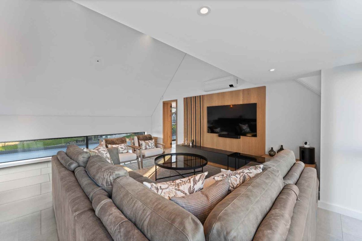 Modern living room featuring a timber feature wall, split-system air conditioning, recessed downlights, and large horizontal windows providing natural light.