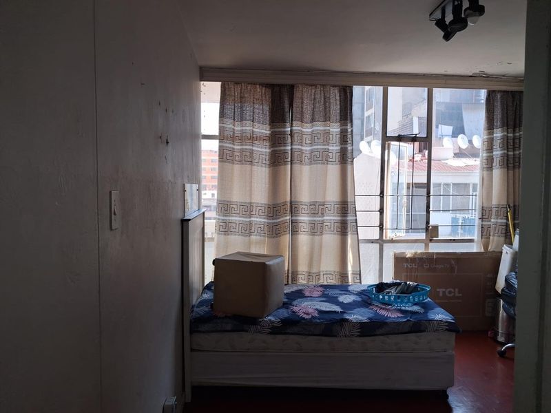 A bedroom featuring a large window with natural light and ceiling-mounted track lighting, requiring cosmetic updates to the walls and ceiling.