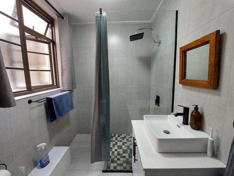 Modern bathroom featuring a walk-in shower with glass screen, contemporary vessel sink vanity, and neutral wall tiling.