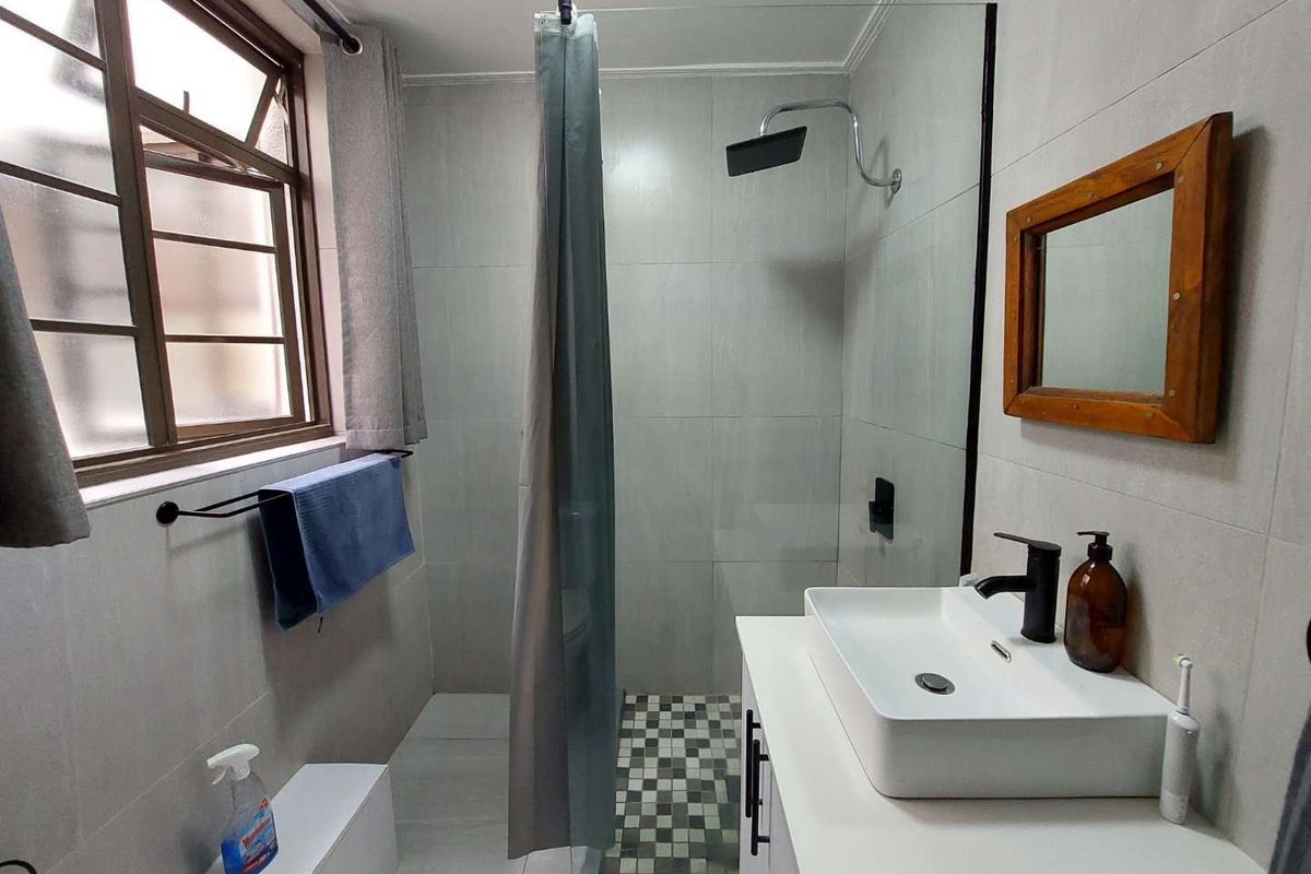 Modern bathroom featuring a walk-in shower with glass screen, contemporary vessel sink vanity, and neutral wall tiling.