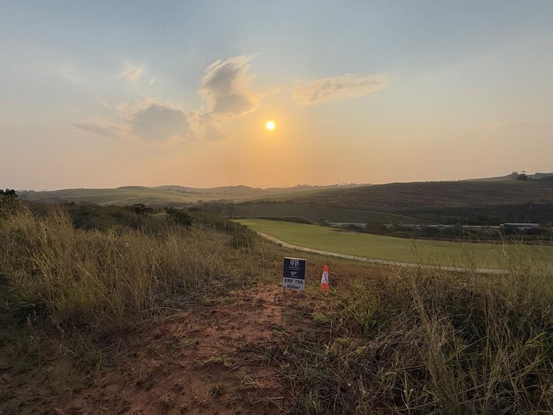 A scenic view of an undeveloped residential plot featuring natural landscape and rolling hills at sunset.
