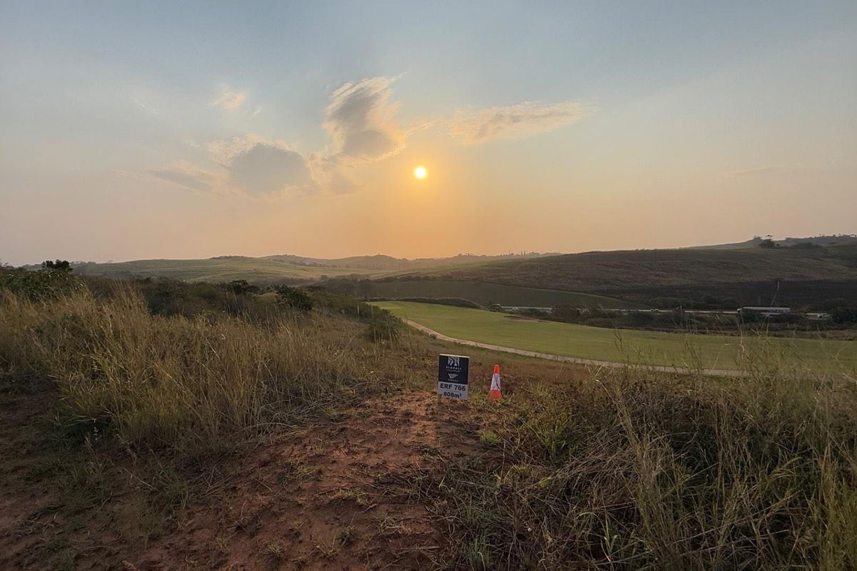 A scenic view of an undeveloped residential plot featuring natural landscape and rolling hills at sunset.