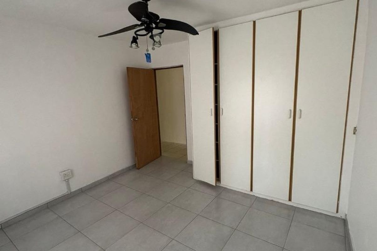 A clean, empty bedroom featuring neutral tiled flooring, built-in white cupboards, and a ceiling fan.