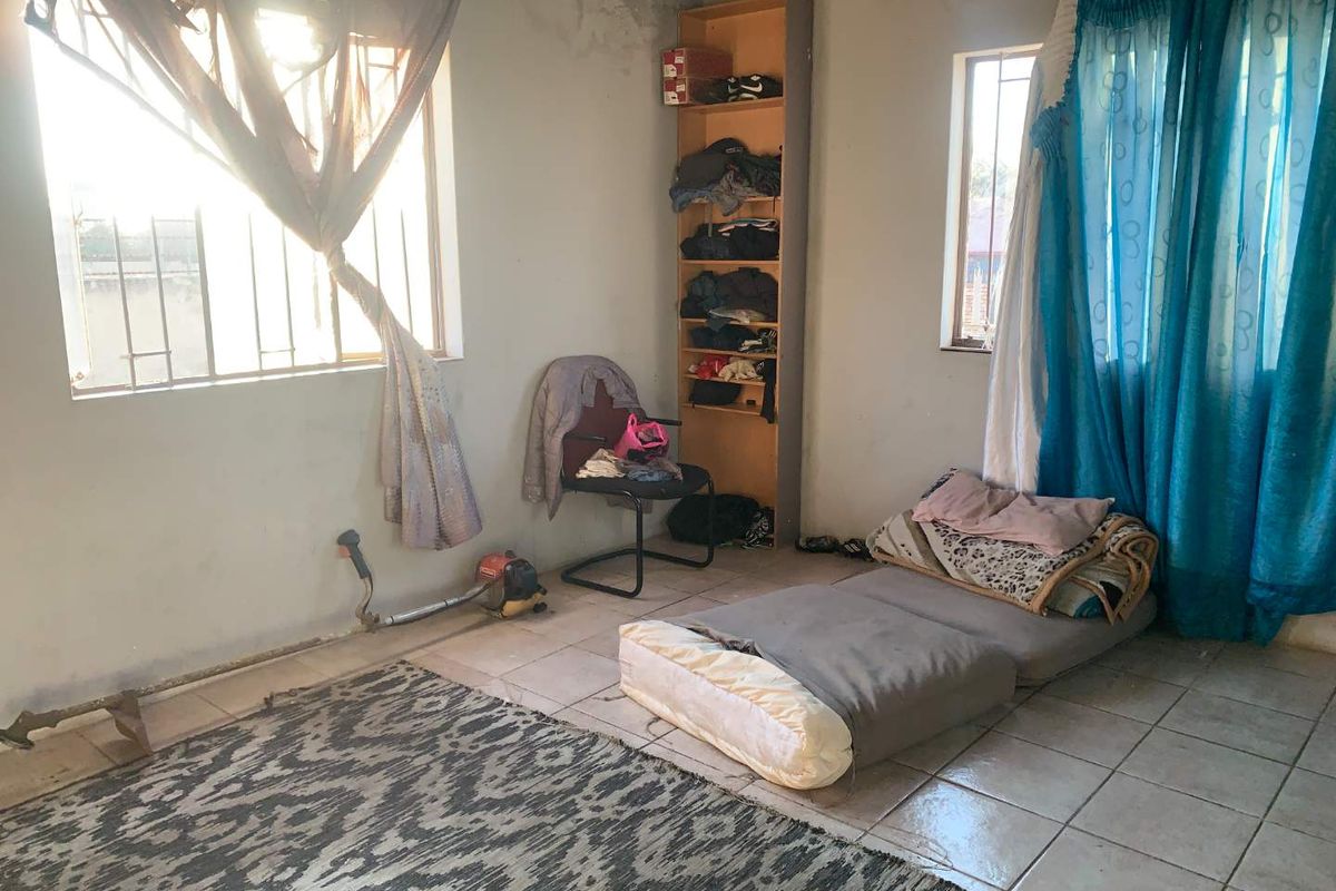 A bedroom space featuring tiled flooring, built-in shelving, and security bars on the windows, requiring cosmetic updates and repairs to wall finishes.