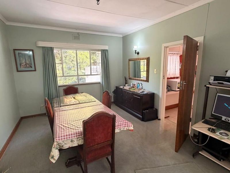 A dining room featuring a large window, coving, and direct access to an adjacent room, offering a functional space with potential for modernization.