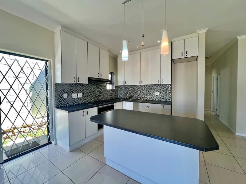 Modern kitchen featuring white cabinetry, dark countertops, a central island, mosaic tile backsplash, and tiled flooring, with direct access to an outdoor area.