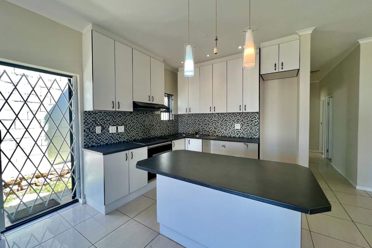Modern kitchen featuring white cabinetry, dark countertops, a central island, mosaic tile backsplash, and tiled flooring, with direct access to an outdoor area.
