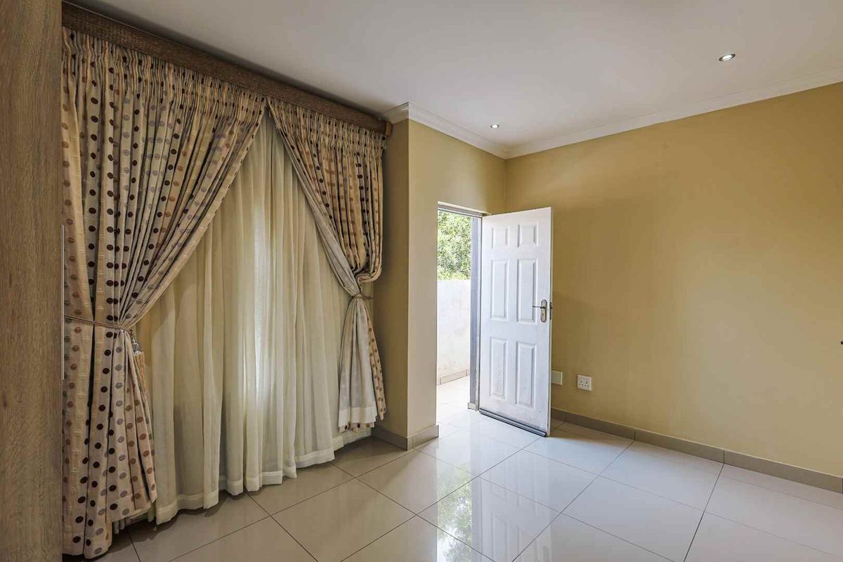 A bright bedroom featuring tiled flooring, recessed ceiling lighting, and direct access to an outdoor area through a panelled door.