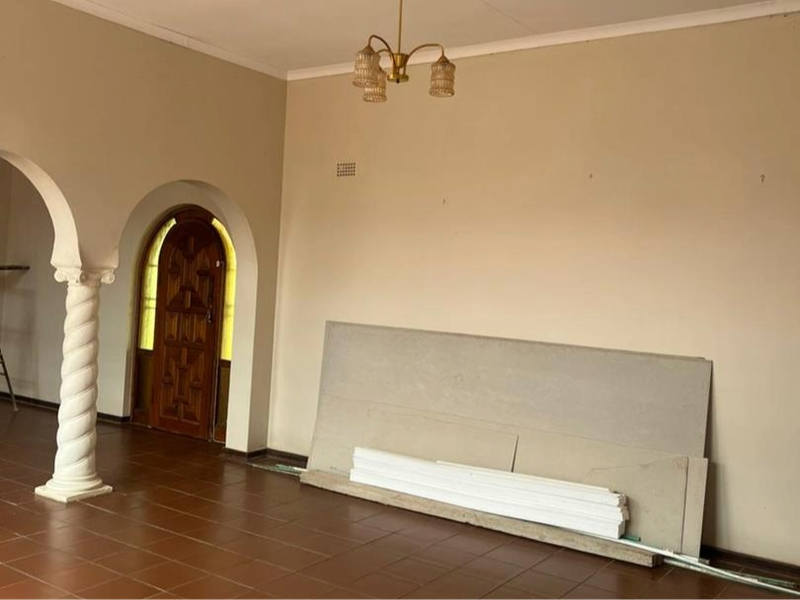 Spacious living area featuring classic arched doorways, decorative spiral columns, and tiled flooring, offering a versatile layout for renovation.