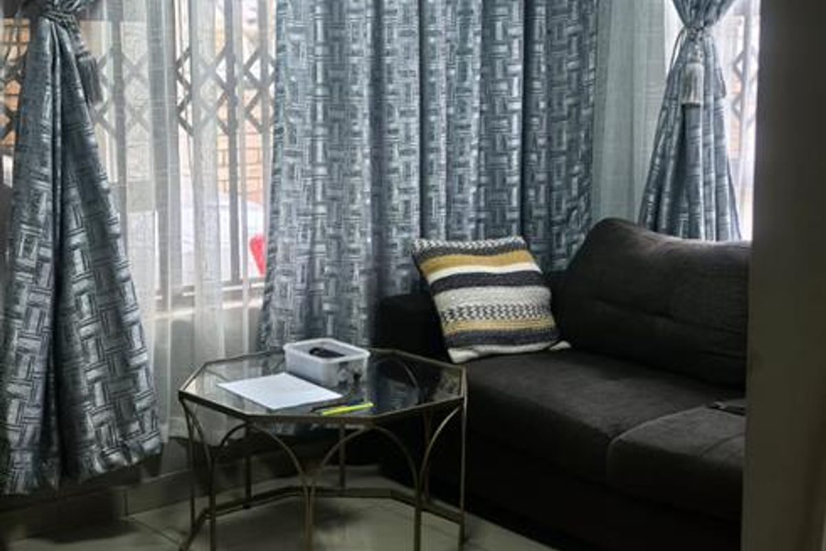 A compact living room featuring polished floor tiles, a central ceiling light, and large windows fitted with security gates.