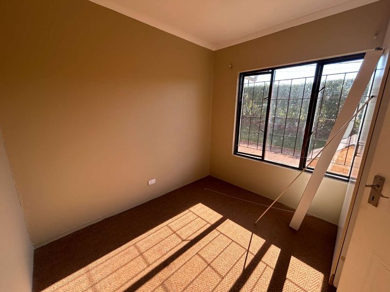An empty bedroom featuring carpet flooring, neutral wall paint, and a window fitted with security burglar bars.