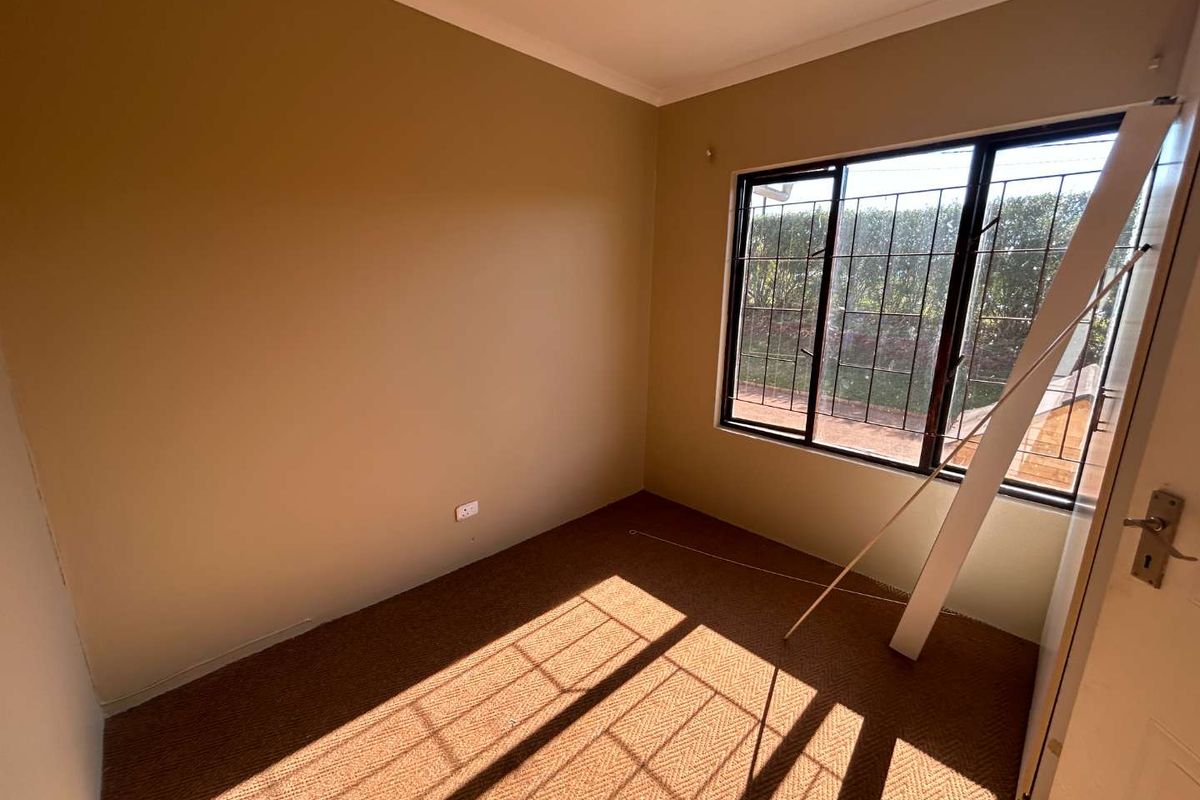 An empty bedroom featuring carpet flooring, neutral wall paint, and a window fitted with security burglar bars.