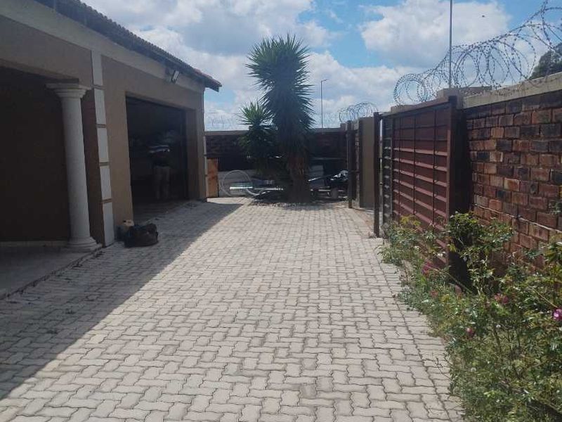 A paved driveway leading to a garage entrance, featuring a brick boundary wall with security razor wire and a decorative column.