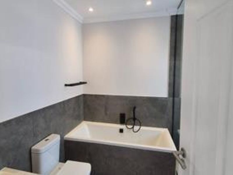 A modern bathroom featuring a built-in bathtub, dark grey tiled wall accents, and contemporary black fixtures.