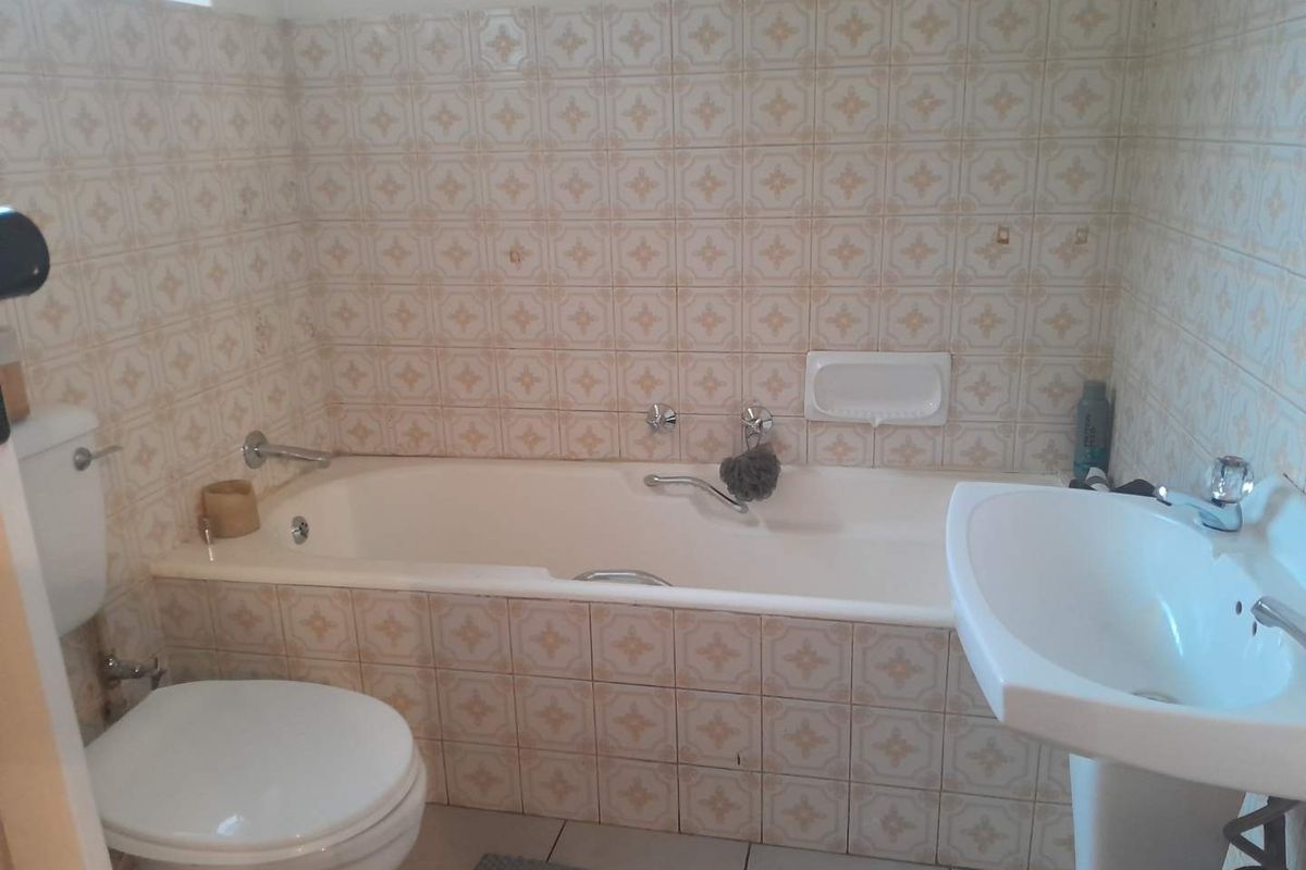A functional bathroom featuring a standard bathtub, pedestal basin, and toilet with dated ceramic wall tiling throughout.