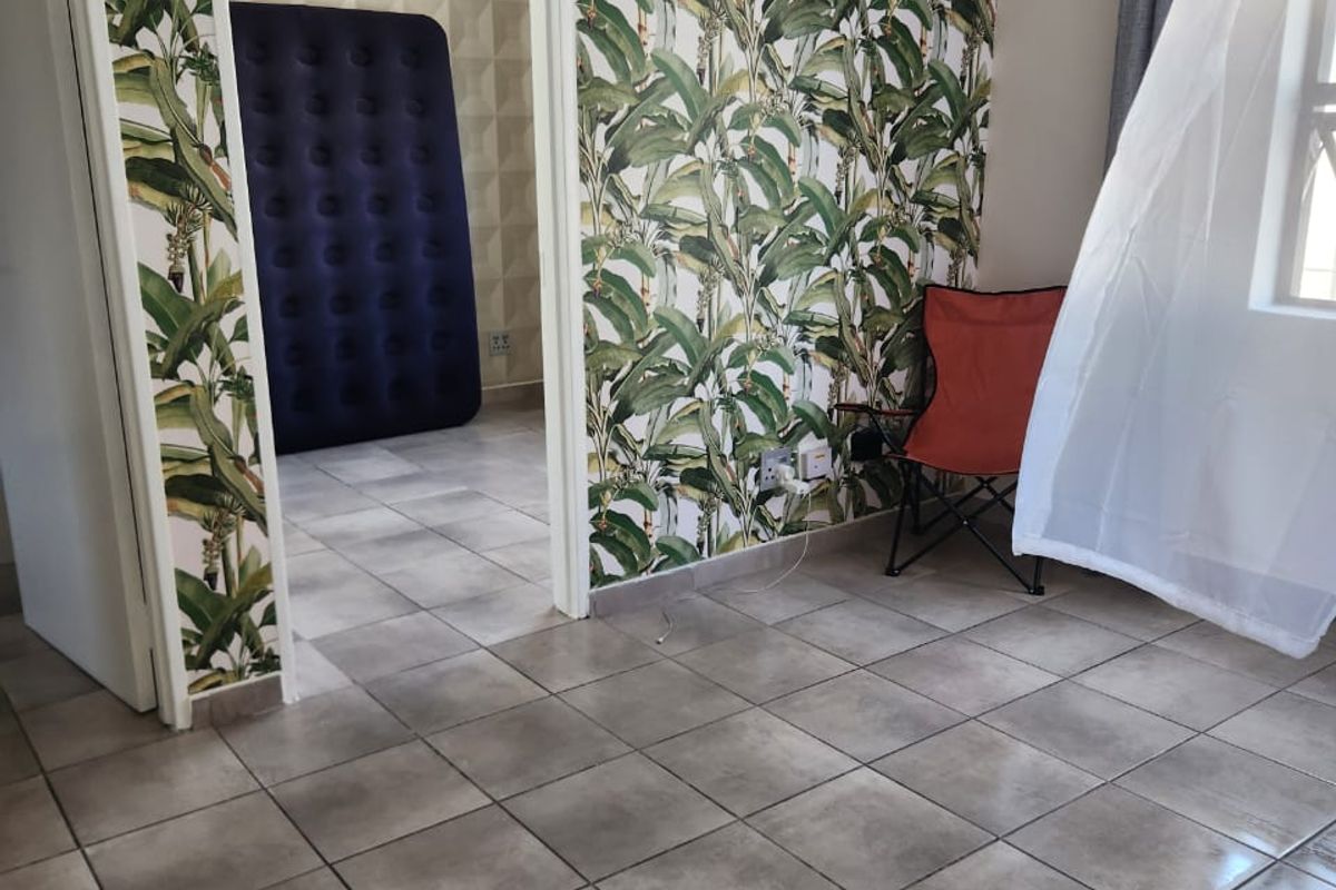 A bedroom featuring tiled flooring and bold botanical wallpaper, with an adjoining room visible through the doorway.