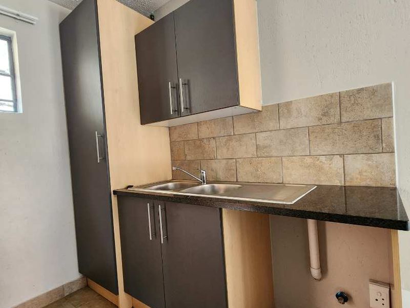 A compact kitchen area featuring built-in cabinetry, a stainless steel sink, tiled backsplash, and ceramic floor tiles, ready for modernization.