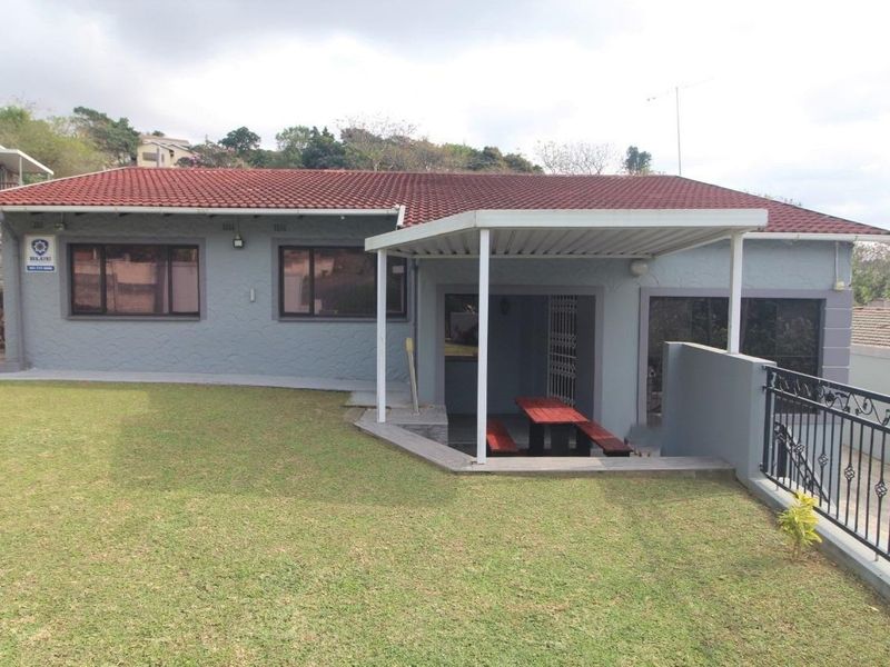 Rear view of the house featuring a covered patio area, well-maintained lawn, and secure perimeter fencing.