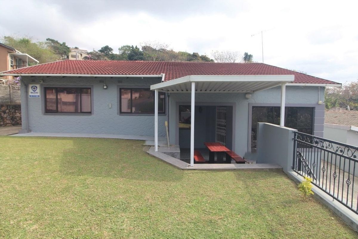 Rear view of the house featuring a covered patio area, well-maintained lawn, and secure perimeter fencing.