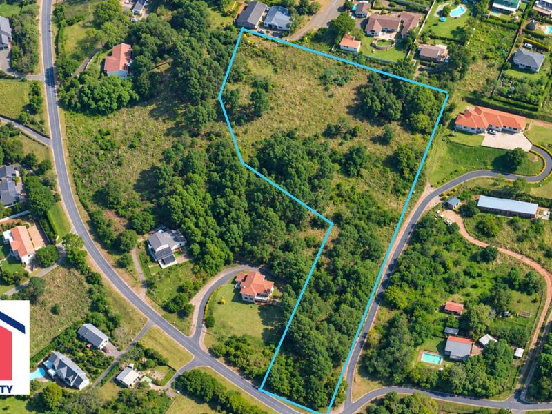 An aerial view of a vacant residential plot featuring natural vegetation and trees, situated within an established neighborhood.