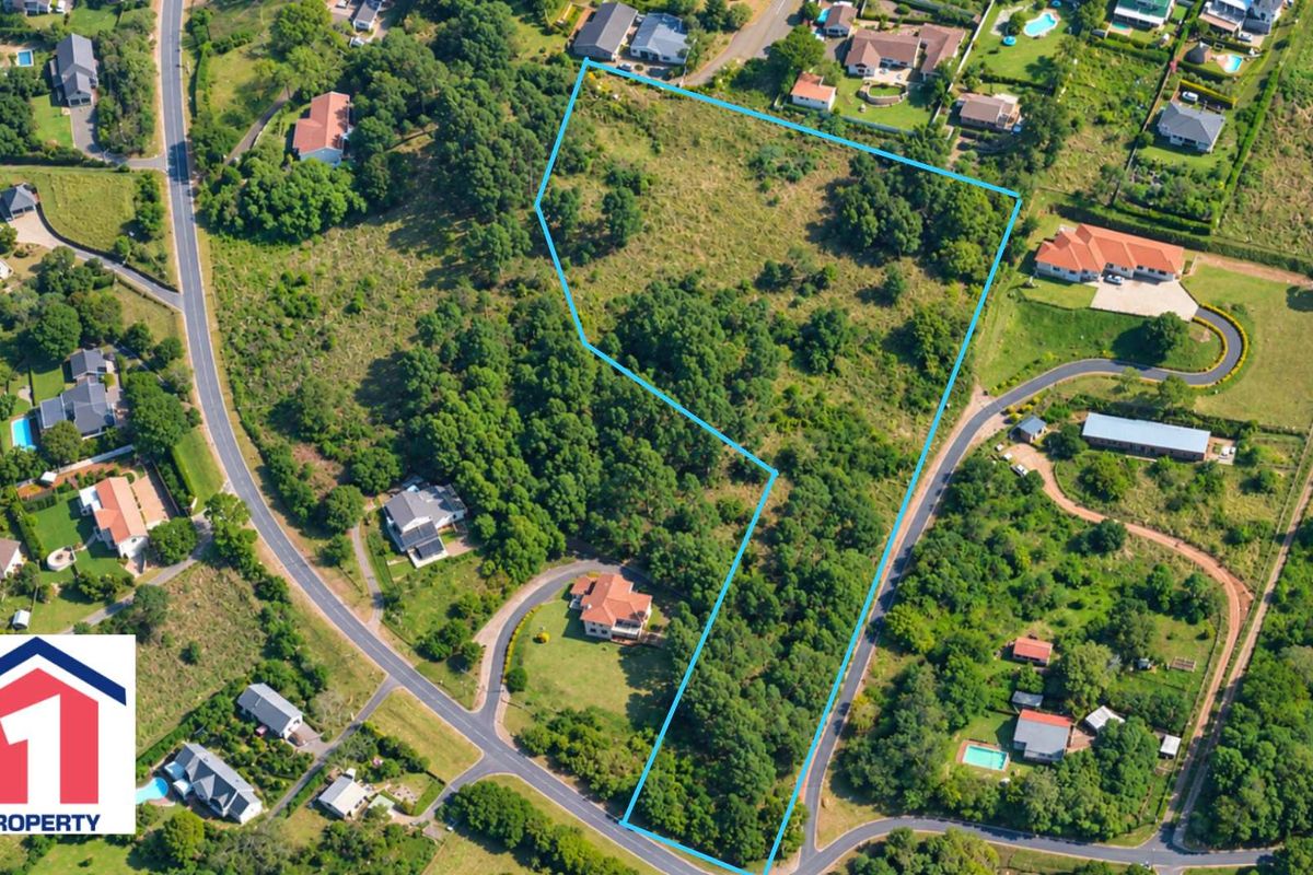 An aerial view of a vacant residential plot featuring natural vegetation and trees, situated within an established neighborhood.