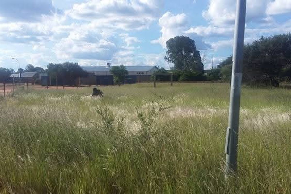 A view of a vacant commercial land plot featuring natural grass cover, perimeter fencing, and an existing utility pole.