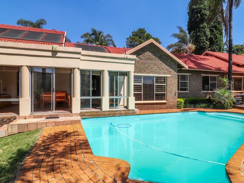 A well-maintained outdoor pool area featuring brick paving, a covered patio space, and a tiled roof with integrated solar heating panels.