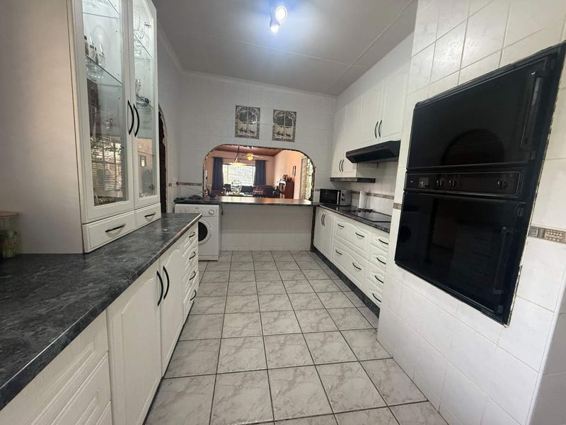 A functional kitchen featuring white cabinetry, dark laminate countertops, built-in double oven, and a convenient pass-through window connecting to the living area.