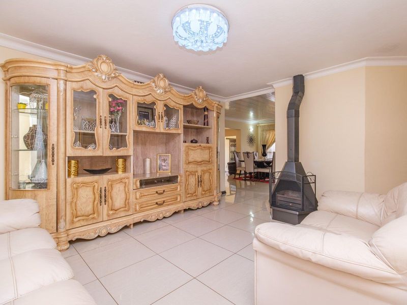 A spacious living room featuring tiled flooring, a freestanding fireplace, and decorative ceiling lighting, with an open flow into the adjacent dining area.