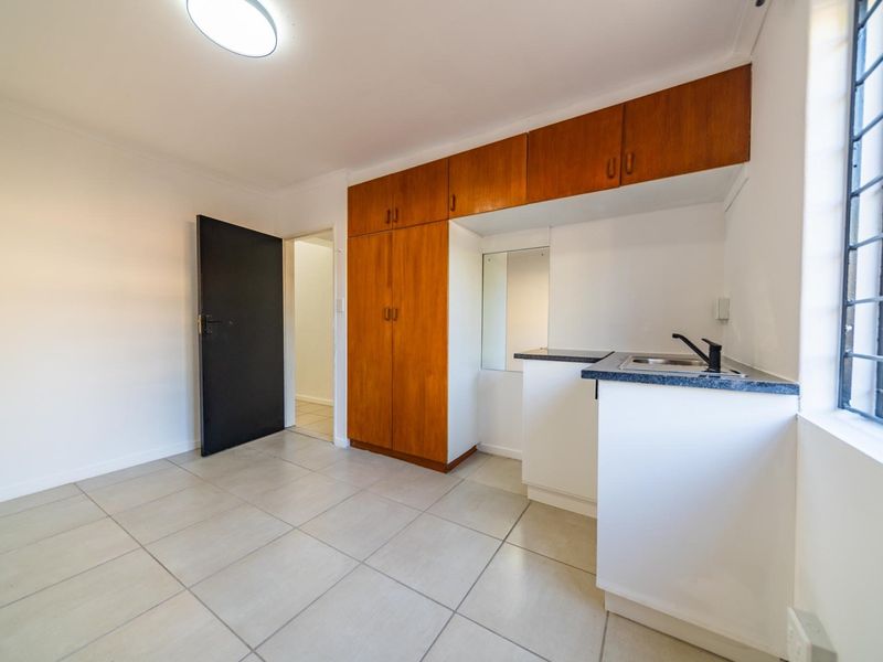 A compact kitchen area featuring built-in wooden cabinetry, a sink, and tiled flooring, offering a functional space ready for personalization.