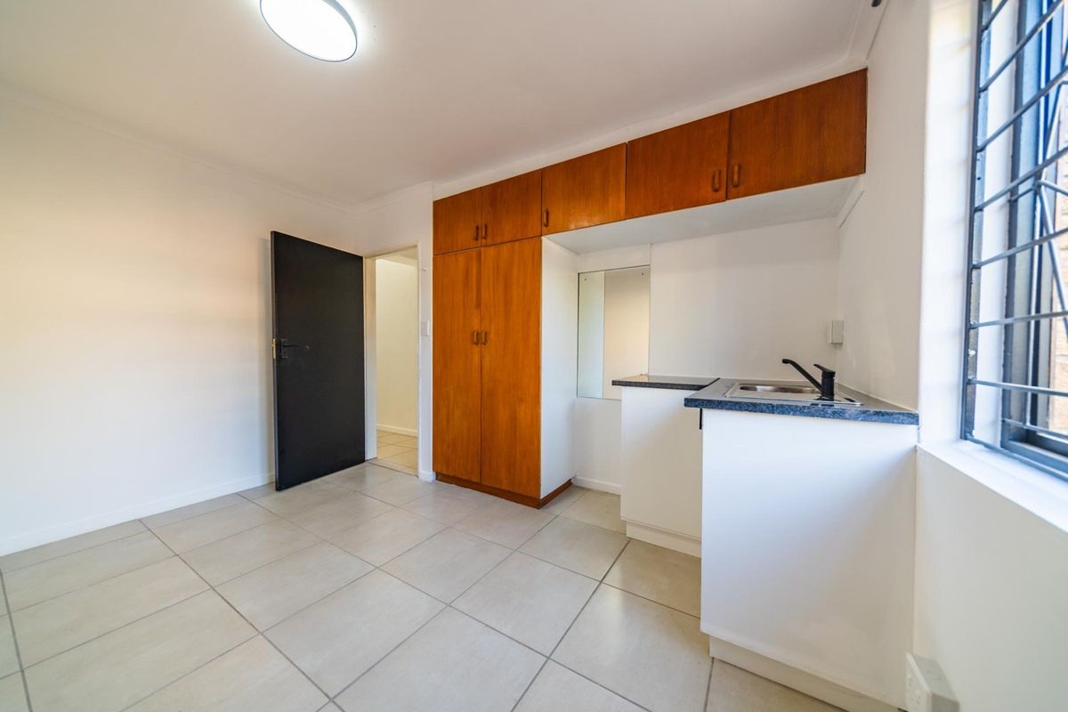 A compact kitchen area featuring built-in wooden cabinetry, a sink, and tiled flooring, offering a functional space ready for personalization.