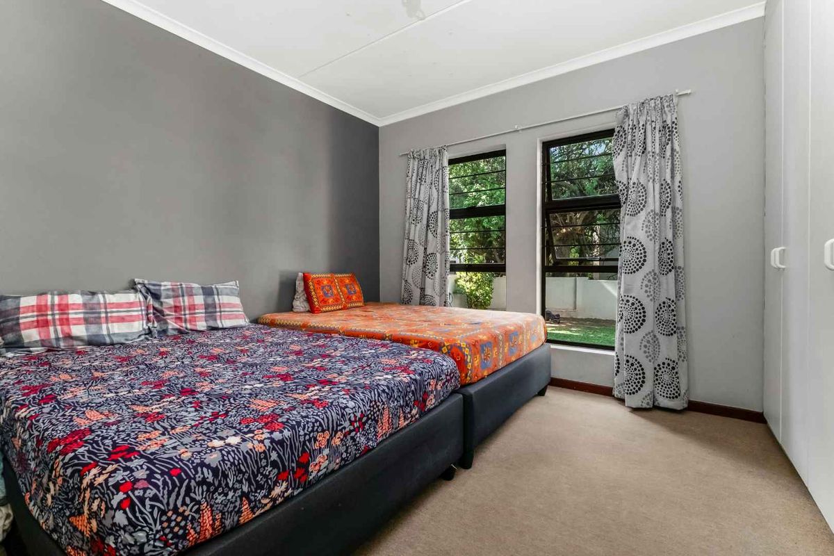 A bedroom featuring neutral grey walls, carpeted flooring, and built-in cupboards, with large windows providing natural light and garden views.